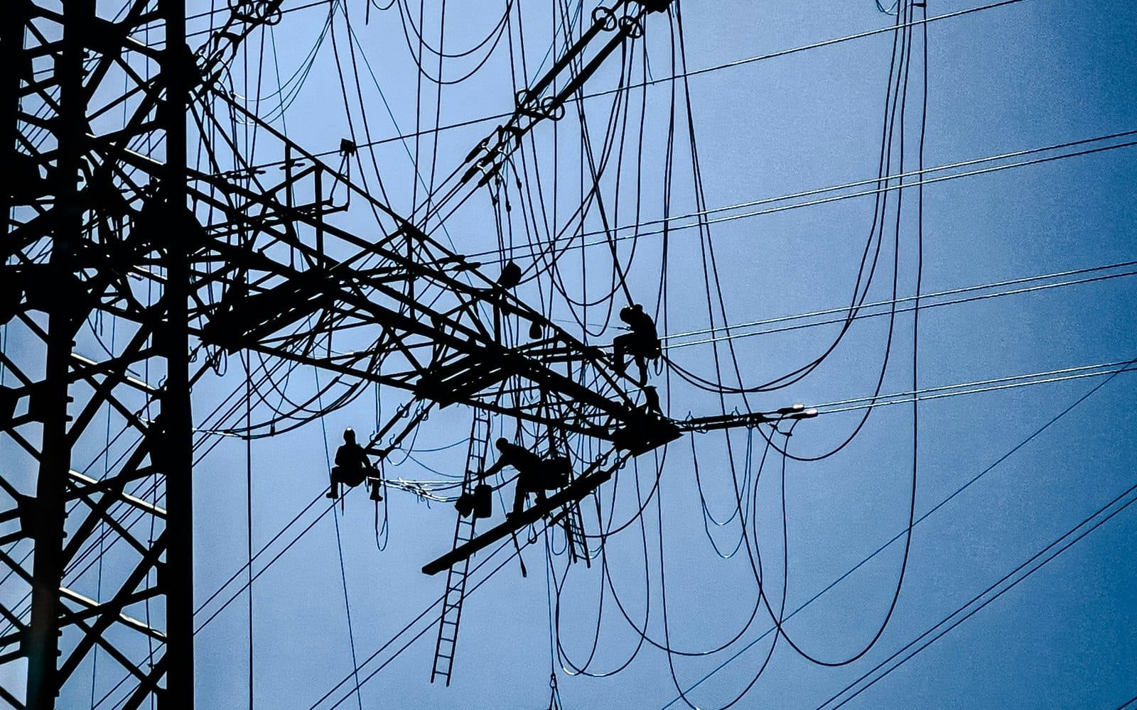 Enerji hattı direğinde bakım yapan teknisyenler; gökyüzüne karşı siluet